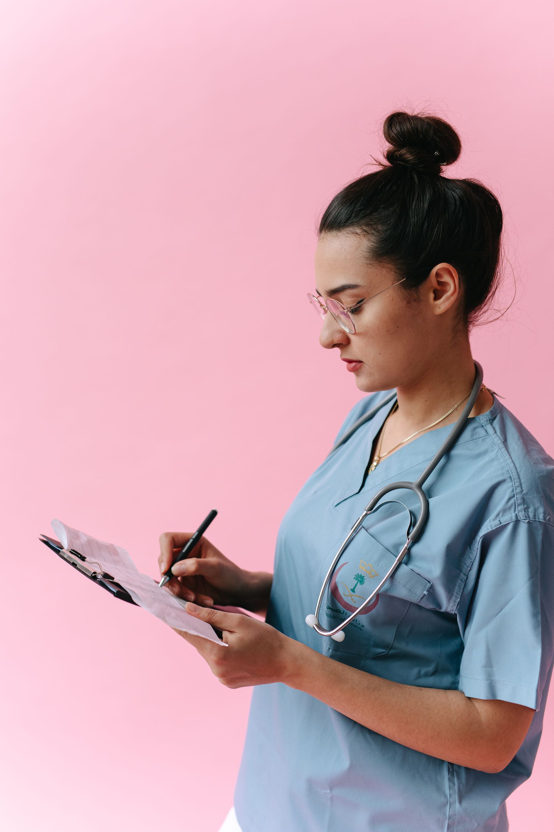 Healthcare professional in blue scrubs writing on a clipboard